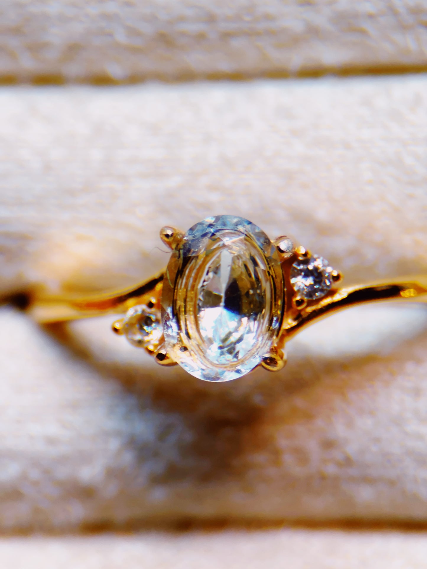 Gold ring with a large central gemstone and smaller stones on a neutral background