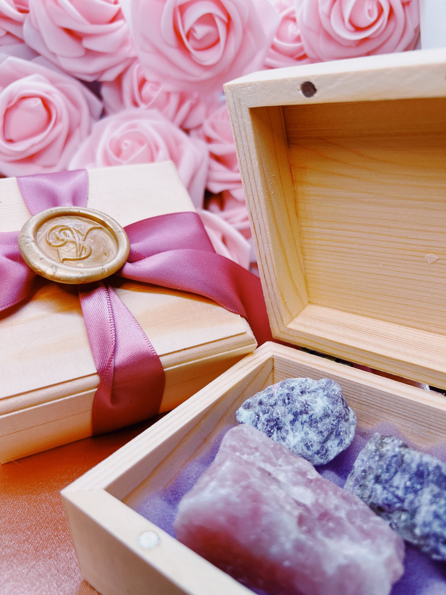 Wooden box with pink ribbon and wax seal, containing purple crystals on a pink rose background