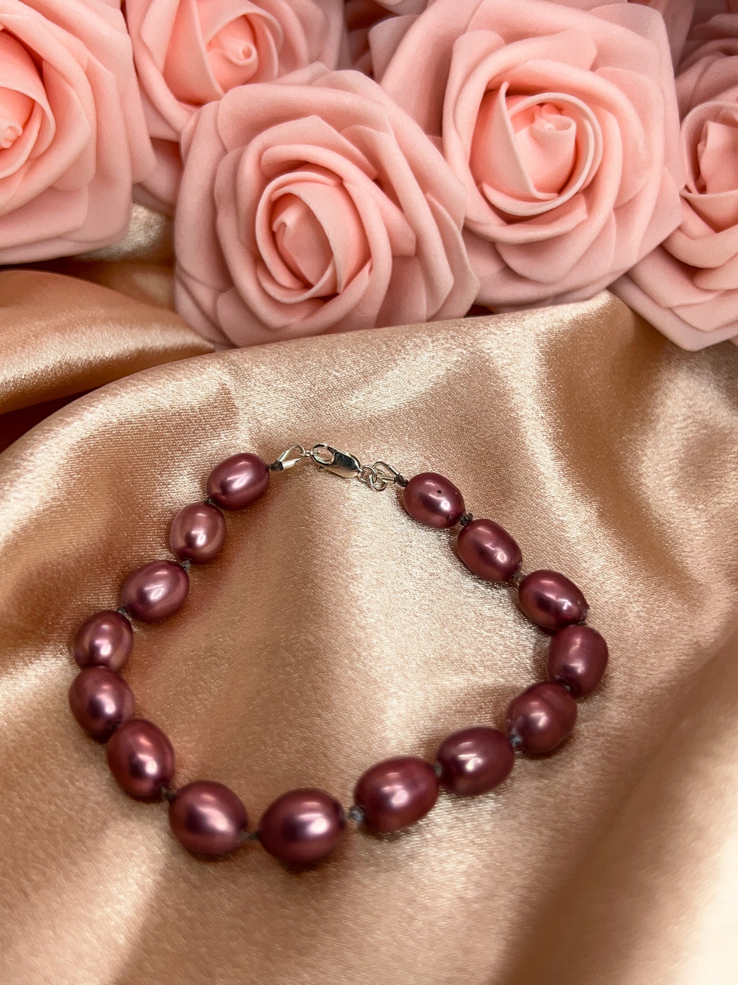 Pearl bracelet on a satin surface with pink roses in the background