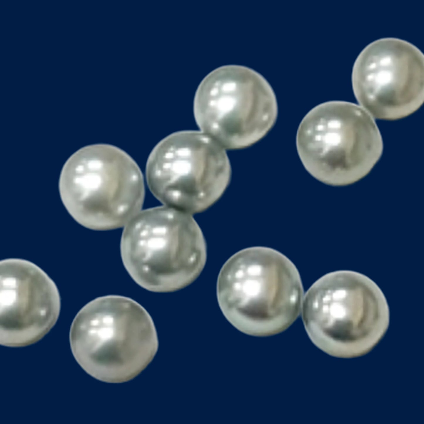 Loose light blue-gray pearls scattered across a deep navy background, each showing bright white reflections and soft, rounded highlights.