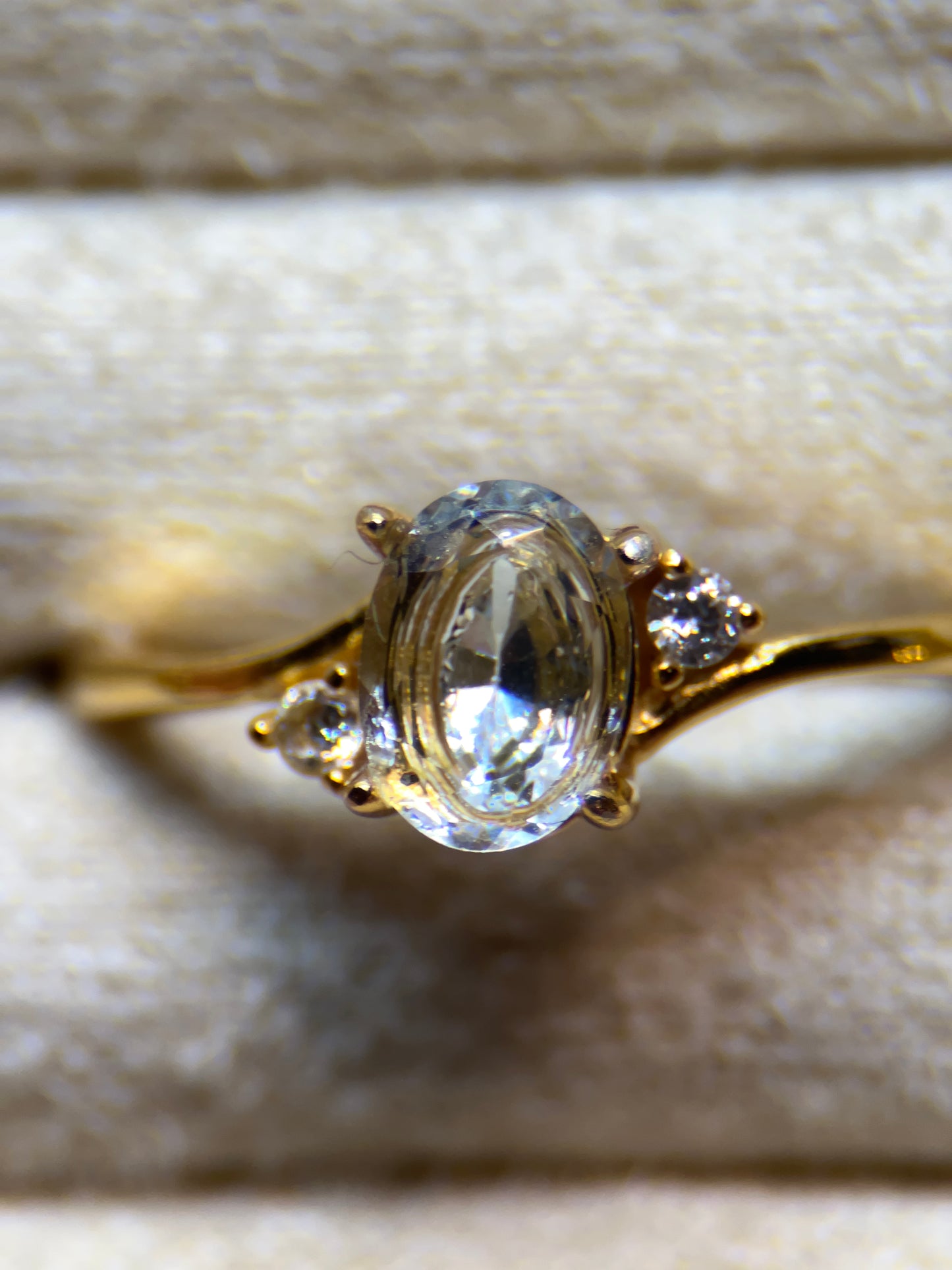 Gold ring with a clear gemstone on a textured beige background