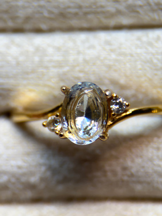 Gold ring with a clear gemstone on a textured beige background