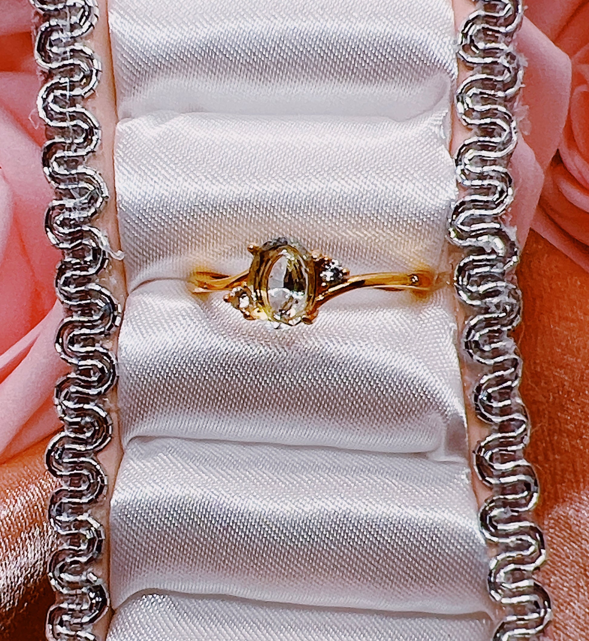 Gold ring with a green gemstone on a white cushion, framed by silver chain borders.