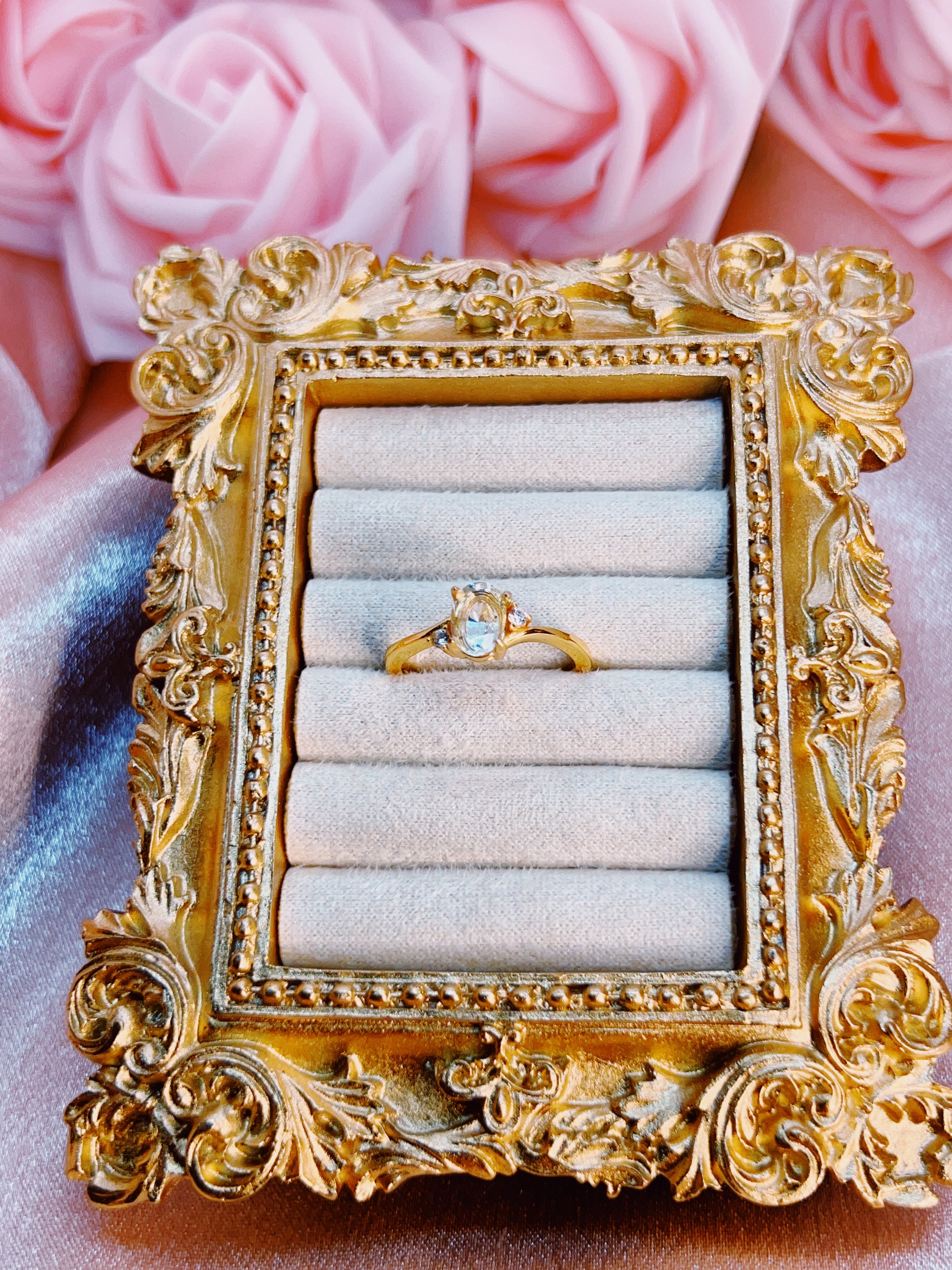 Decorative gold ring box with a ring inside, pink roses in the background