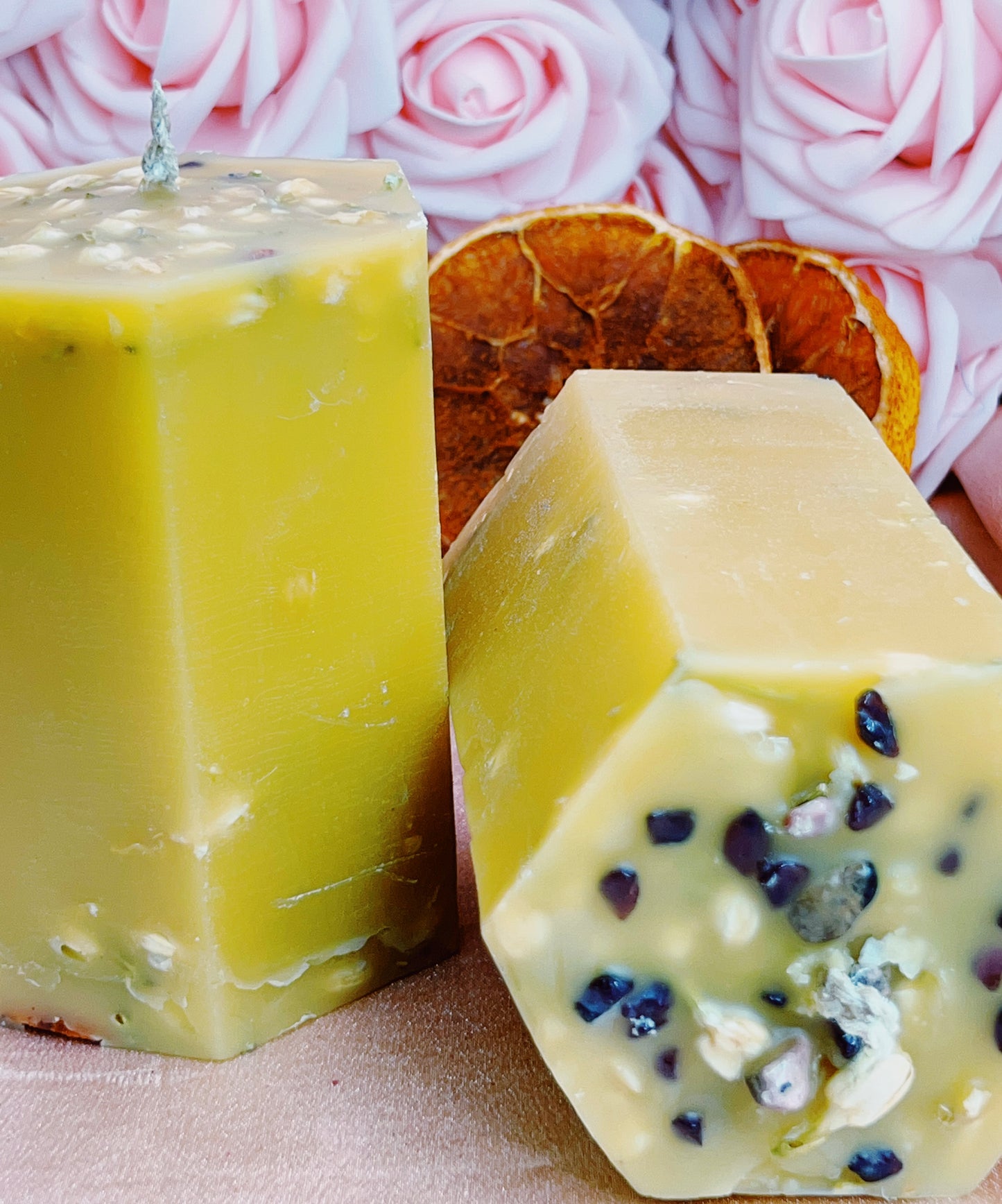 Two hexagonal candles, one yellow and one with visible seeds, against a pink rose background.