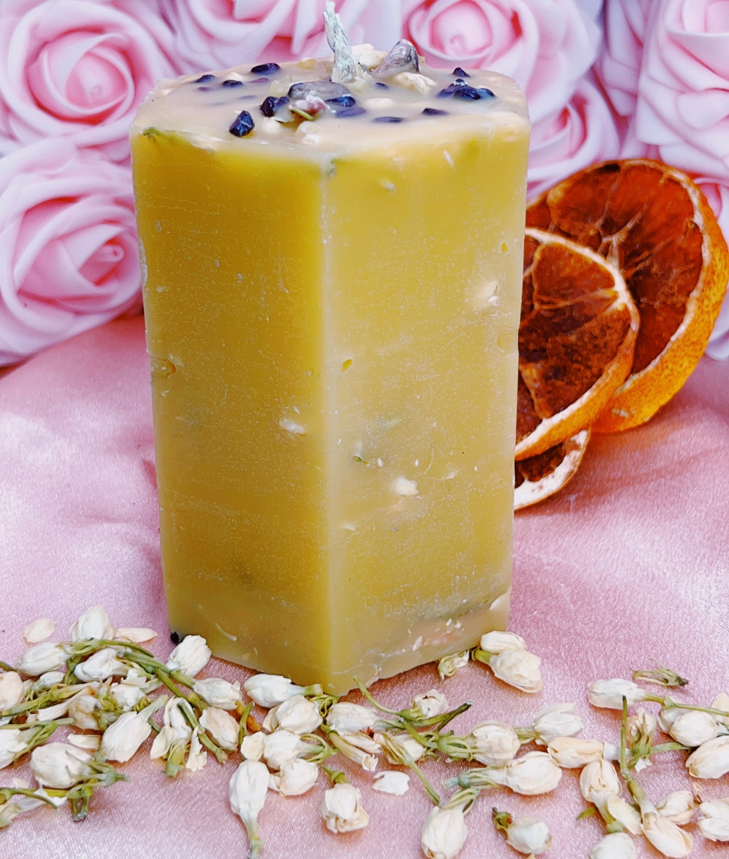 Beeswax with specks on a pink surface with flowers and an orange slice.