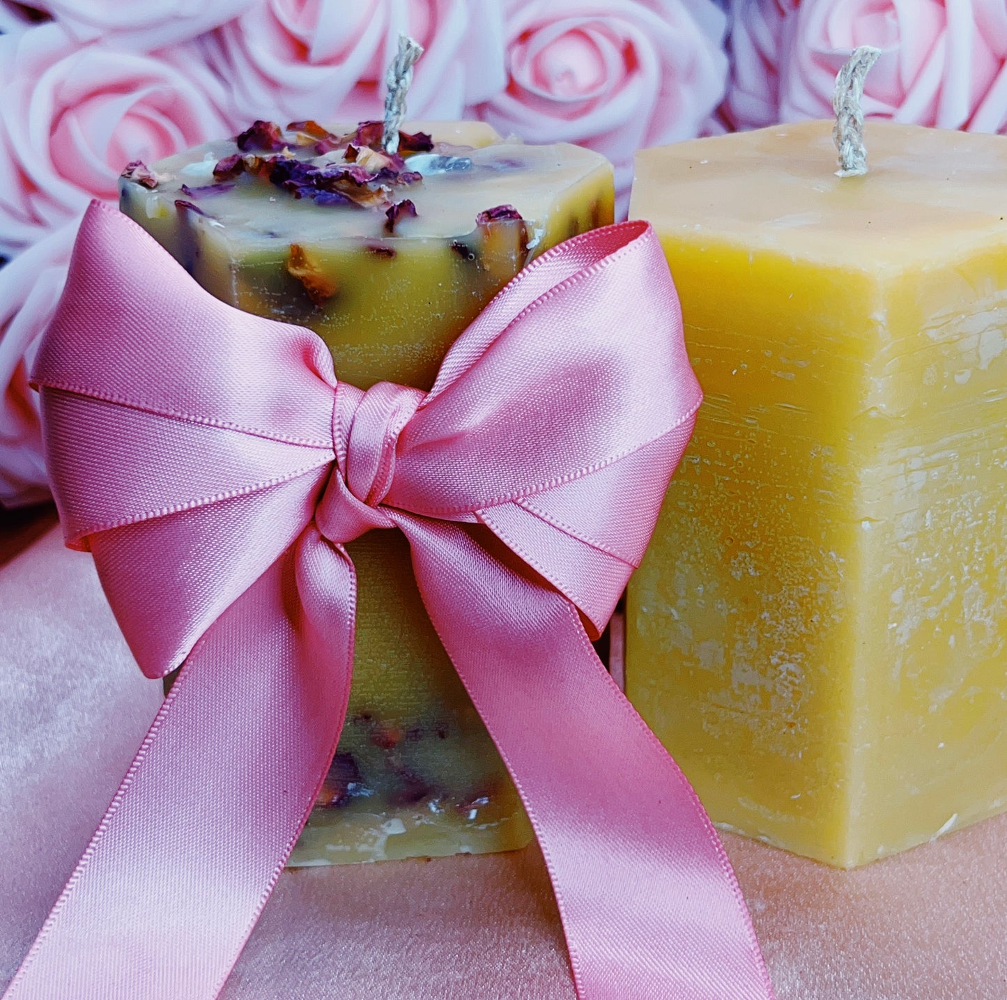 Two square candles with pink ribbons against a floral background