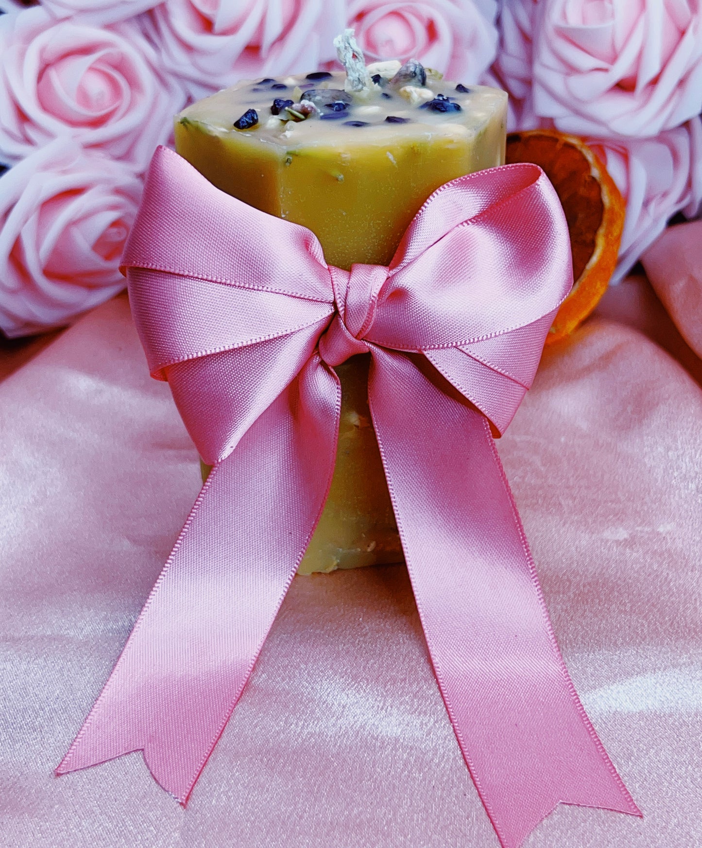 Bar of soap with a pink ribbon on a pink surface with pink roses in the background
