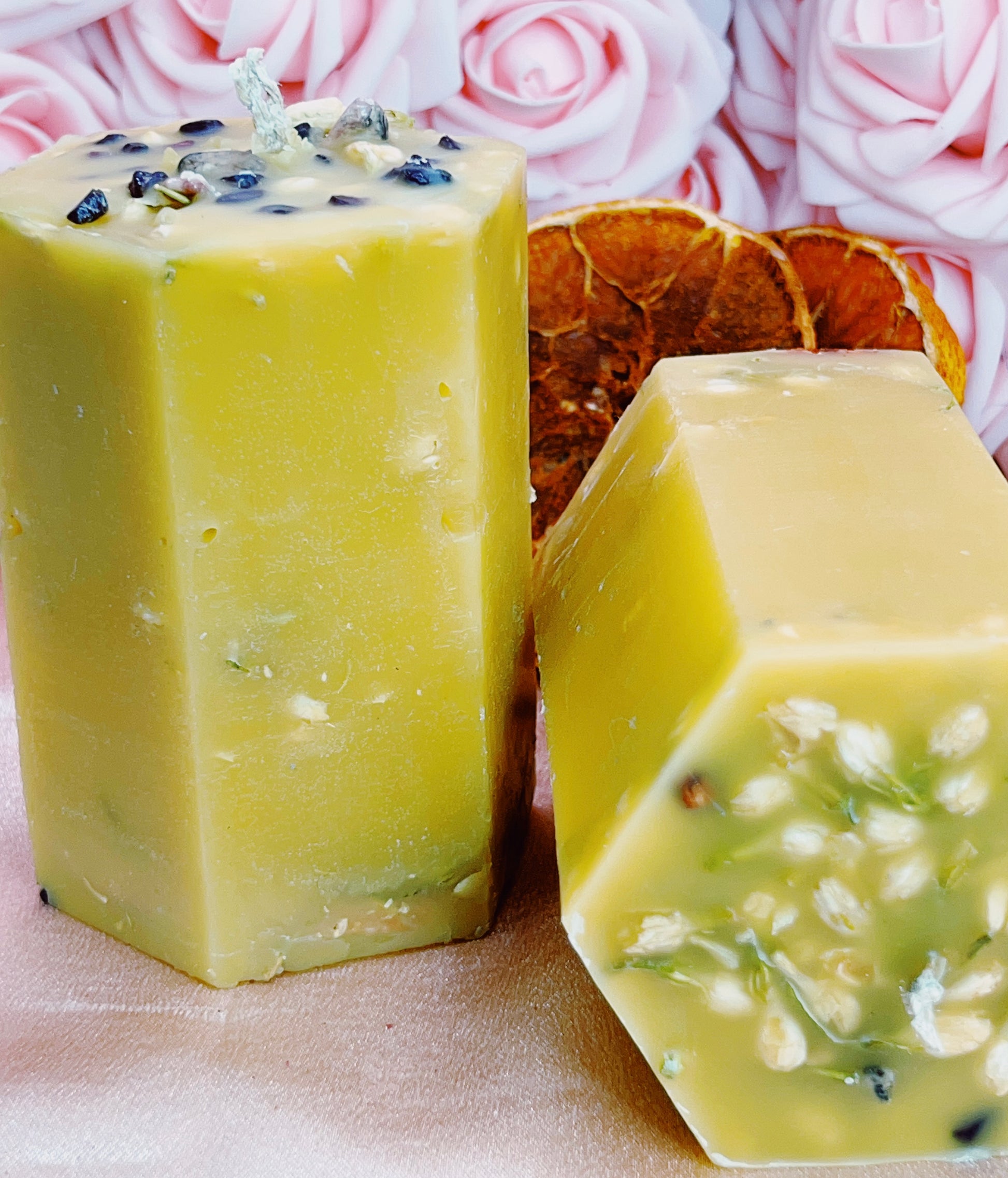 Two hexagonal beeswax candles with visible herbs on a pink floral background