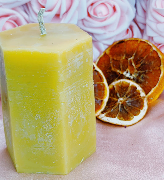 Yellow candle with dried oranges and pink flowers in the background