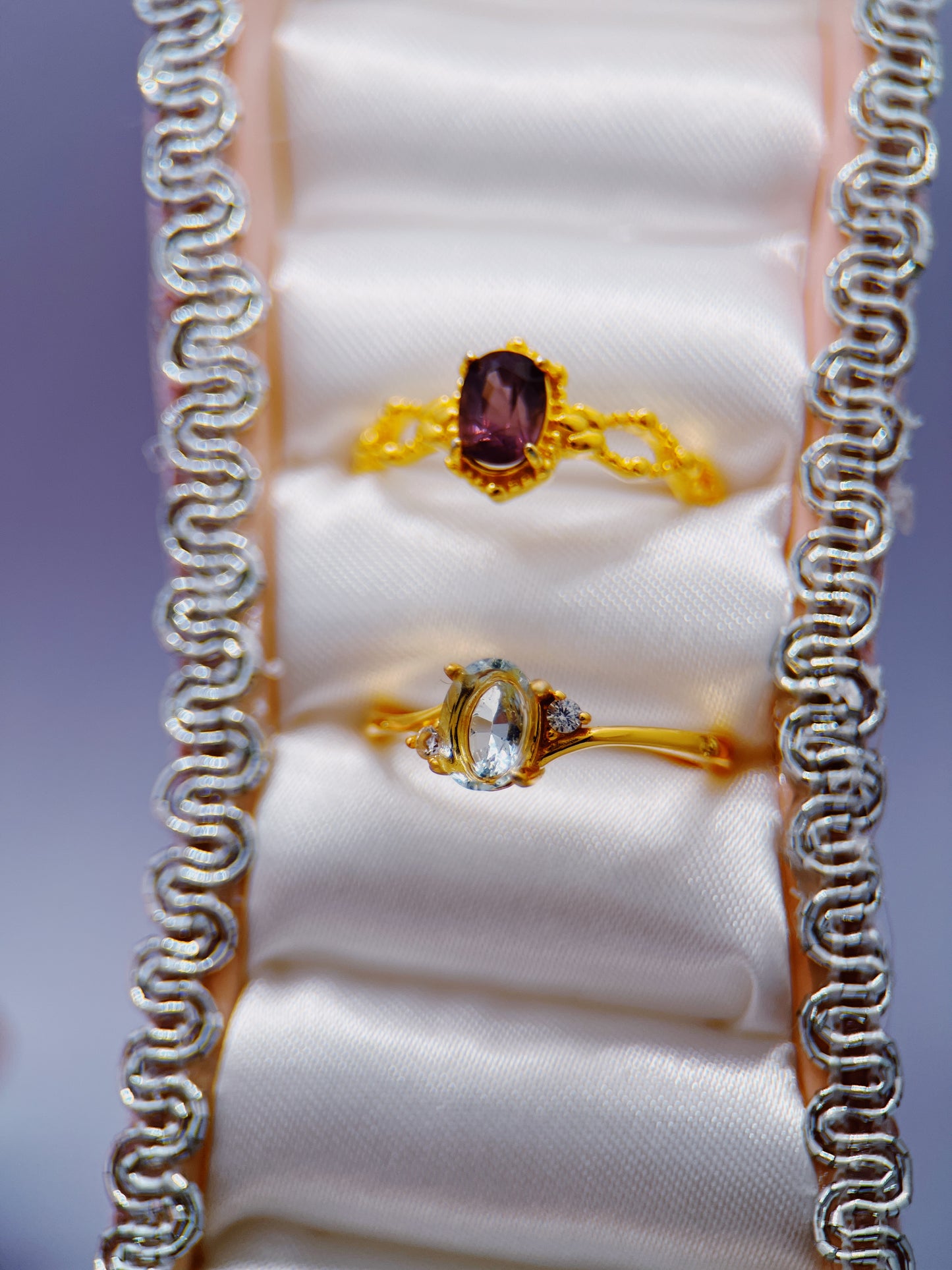 Two gold rings with gemstones on a white cushion inside a jewelry box.