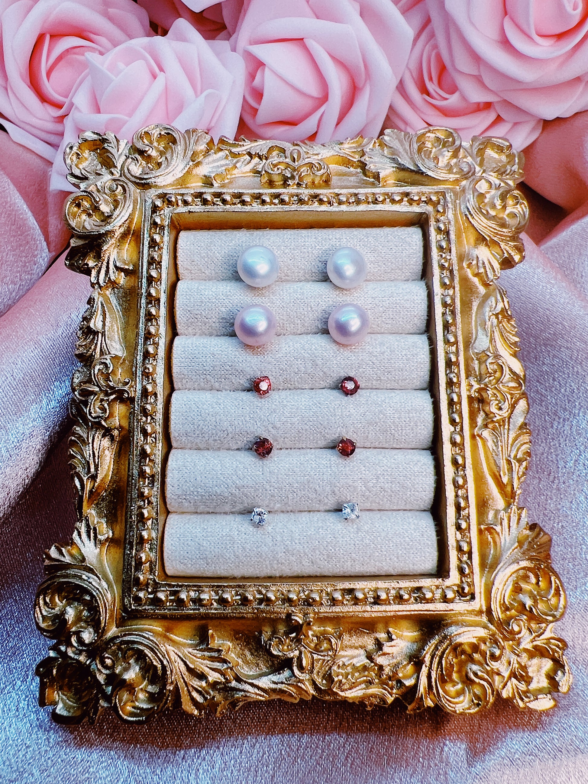 Decorative gold jewelry holder with earrings against a pink floral background