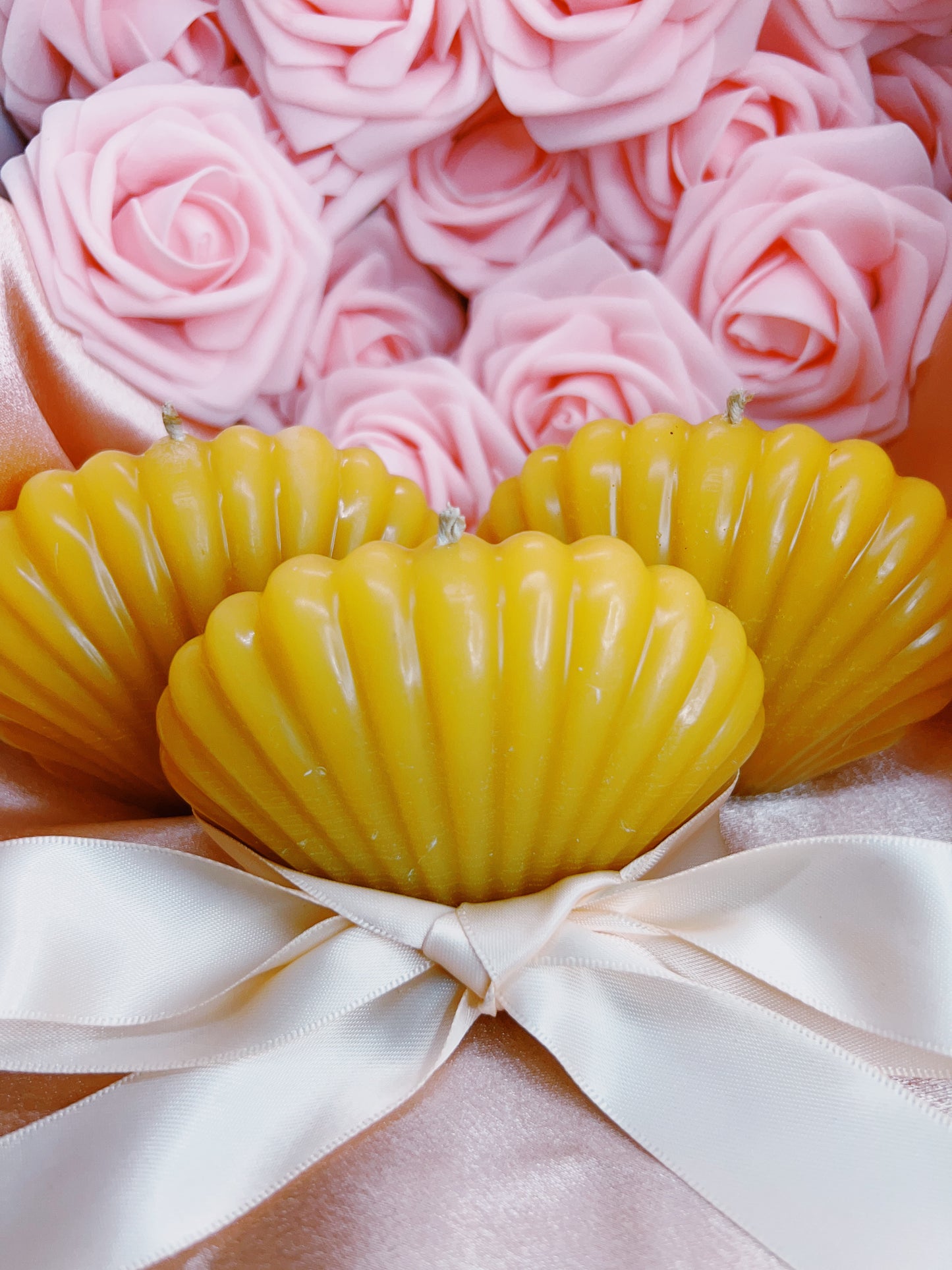 Two yellow shell-shaped candles with pink roses in the background