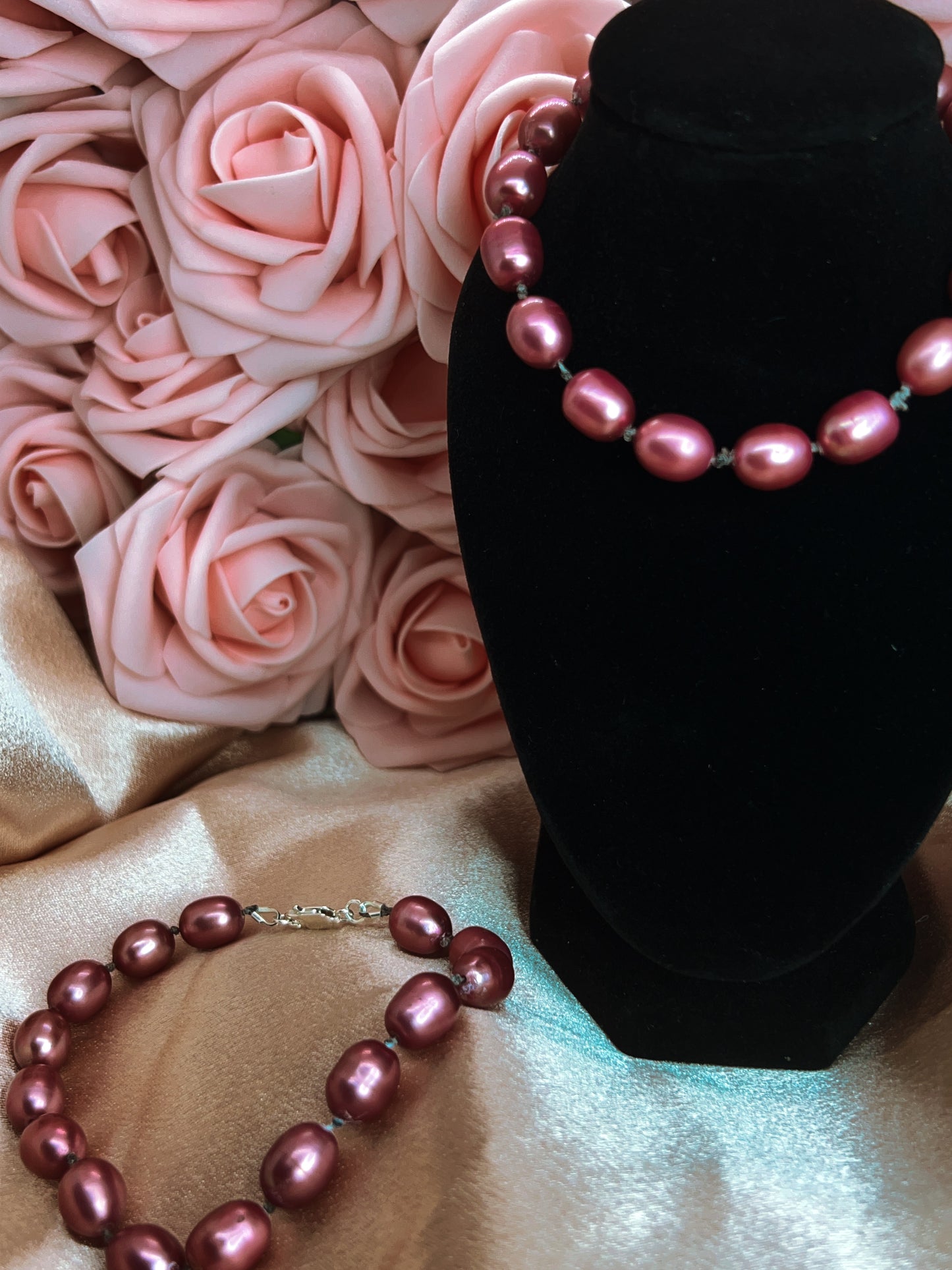 Pink pearl necklace on a black stand with pink roses in the background
