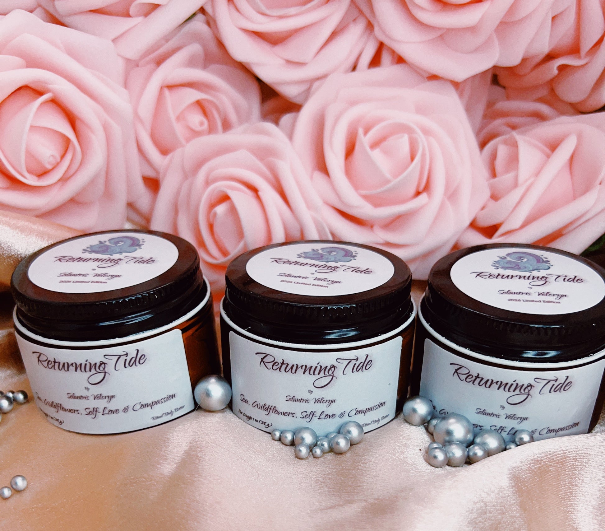 Three jars of 'Returning Tide' body butter on a pink fabric background with pink roses.