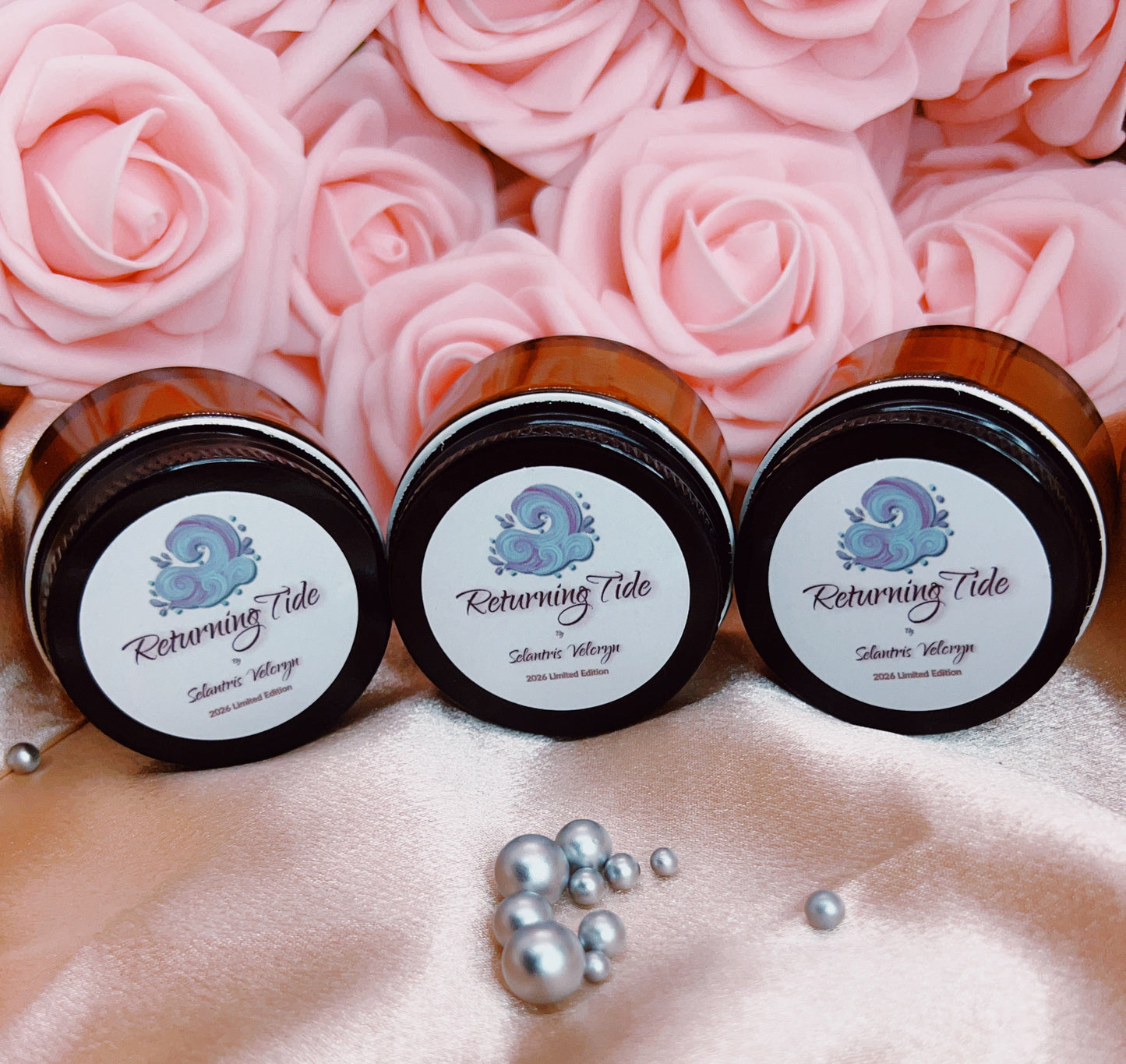 Three jars labeled 'Returning Tide' on a pink fabric background with pink roses.