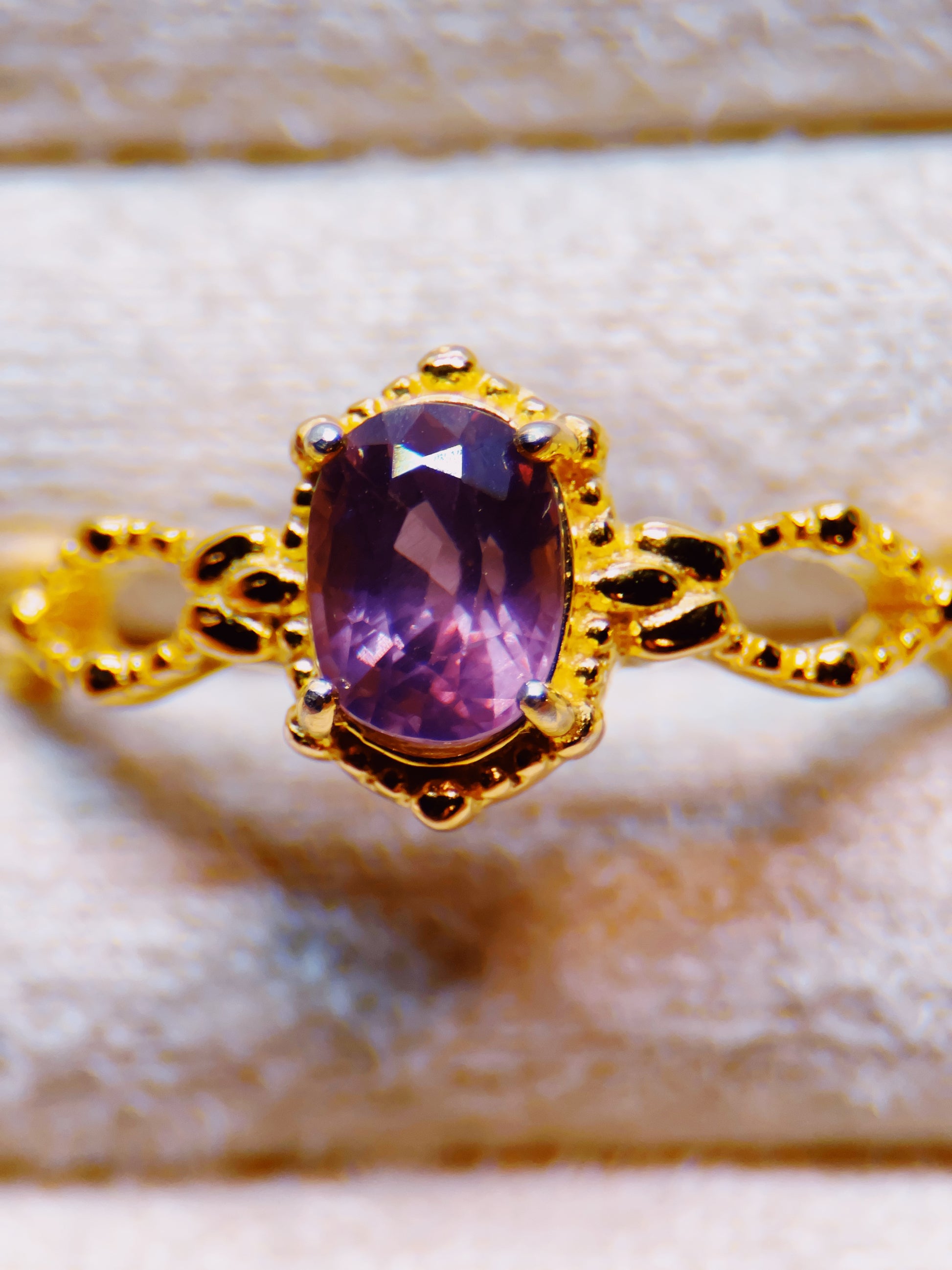 Gold ring with a purple gemstone on a light wooden surface