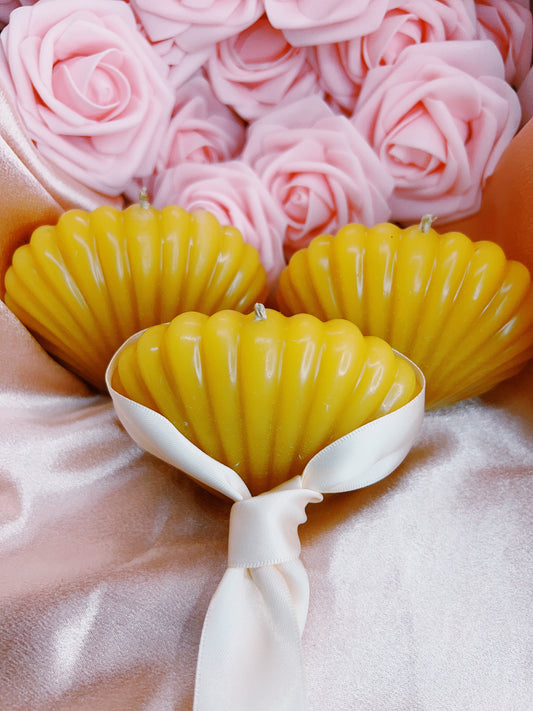 Yellow shell-shaped candles with a white ribbon on a pink floral background